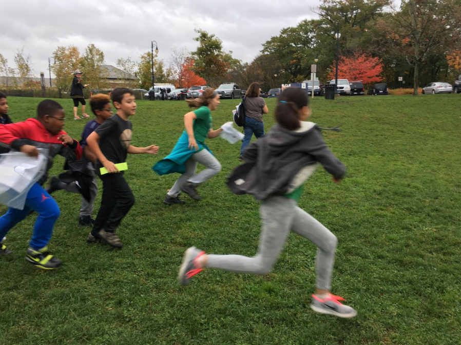 Children running across a park field carrying maps at the start of a Score-O